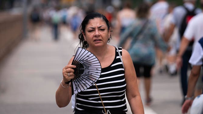 A person uses a hand fan as they walk across Brooklyn Bridge on July 15, 2024 in New York City.