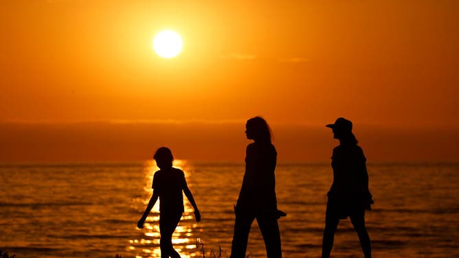 People walk along the coast as the sun sets on the Pacific Ocean at Windansea Beach in La Jolla during a summer heat wave on July 23, 2024 in San Diego, California.