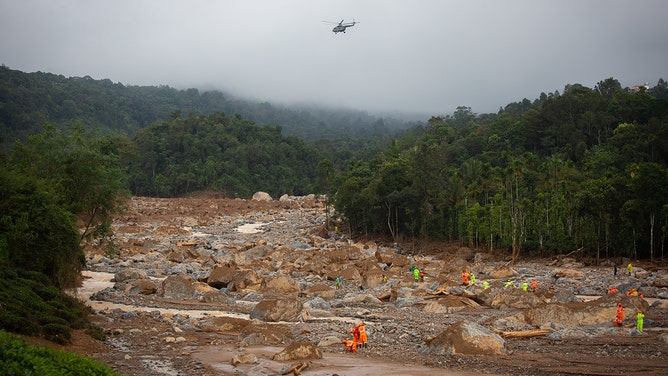 Rescue personnel look for survivors through debris as an Indian Air Force helicopter flies overhead at the site of the landslide on July 31, 2024 in Mundakkai village, India.