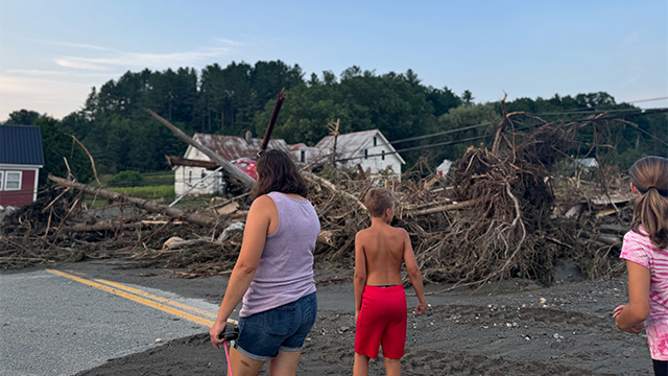 A massive pile of debris is seen as residents of Lyndonville, Vermont, look on after catastrophic flooding on Tuesday, July 30, 2024.