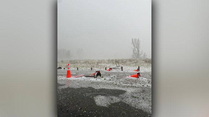 Several traffic cones and a stop sign lay on the ground after being blown over in a hail storm.