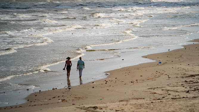 People walk down Galveston Beach.