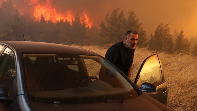 ATHENS, GREECE - AUGUST 12: A man leaves his house during a forest fire in Dione, near Athens, Greece, August 12, 2024. A major fire that broke out in the northeastern town of Varnavas in Greece's Attica region on Sunday is still raging, forcing residents of nearly 10 villages to evacuate in the early hours of Monday after many houses were damaged, local media reported. (Photo by Costas Baltas/Anadolu via Getty Images)