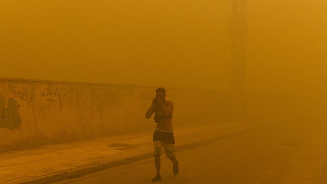 12 August 2024, Greece, Athen: With his upper body bare and a cloth over his mouth, a man walks through a street in Penteli, a municipality in the northern Athens region. Just a few kilometers northeast of the Greek capital, firefighters are battling countless fires over an area of around 200 square kilometers. The government has now asked the EU for support. Photo: Socrates Baltagiannis/dpa (Photo by Socrates Baltagiannis/picture alliance via Getty Images)