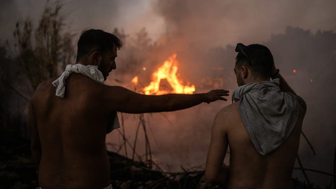 TOPSHOT - Volunteer stand in front of a small pocket of fire as wildfires burn near Penteli, on August 12, 2024. Greece's civil protection authorities ordered the evacuation of several towns in the north-eastern suburbs of Athens, threatened by a violent fire that started the day before and is spreading. European Union said that four countries -- Italy, France, the Czech Republic and Romania -- would send assistance at the request of Greece which is combating a massive wildfire burning through Athens suburbs. (Photo by Angelos TZORTZINIS / AFP) (Photo by ANGELOS TZORTZINIS/AFP via Getty Images)