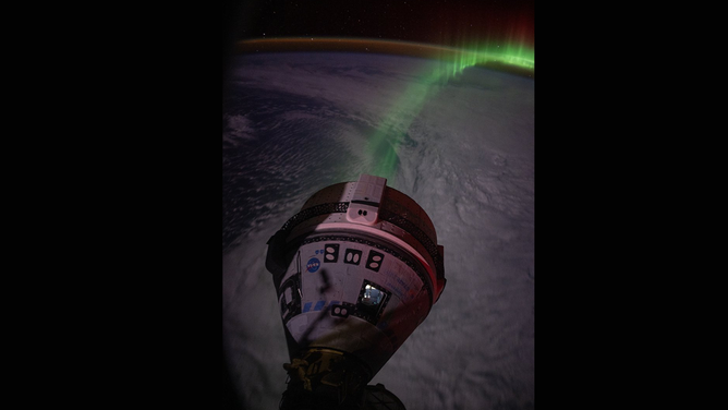 A view of Boeing's Starliner spacecraft as seen from the SpaceX Crew Dragon docked at the space station with a view of aurora lights above Earth.