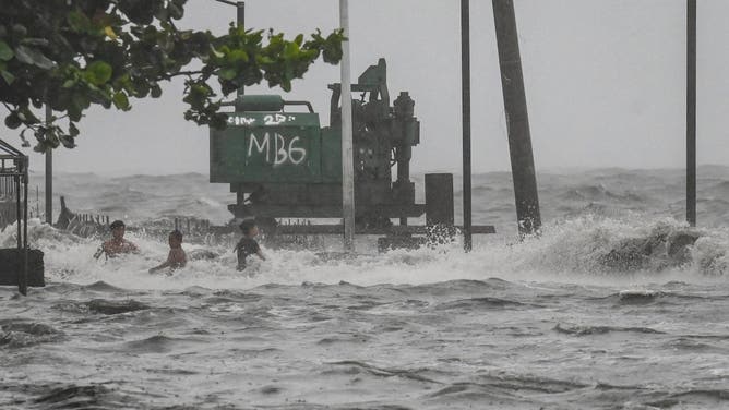 Youths wade in a storm surge along Manila Bay amid heavy rains brought by Tropical Storm Yagi in Manila on September 2, 2024. A tropical storm dumped heavy rain in the Philippines for a second day on September 2, causing floods and landslides that have left at least four people dead, including a nine-month-old girl, officials said. (Photo by JAM STA ROSA / AFP) (Photo by JAM STA ROSA/AFP via Getty Images)