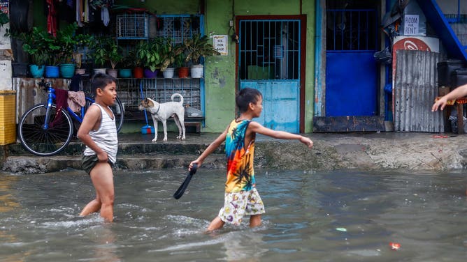 TONDO, MANILA, PHILIPPINES - SEPTEMBER 02: Two children walk past a flooded road in the coastal town of Tondo, where the poorest of the poor reside in, after Typhoon Yagi (Enteng) brought strong winds and heavy rains to the country, in Tondo, Manila, the Philippines, on September 2, 2024. The tropical storm slicing off the coast of the Southeast Asian archipelagos has forced schools and work in some regions to suspend, flights canceled, and caused flooding and landslides. Officials said at least four individuals have died, including a nine-month-old girl in the eastern city of Nega. (Photo by Daniel Ceng/Anadolu via Getty Images)