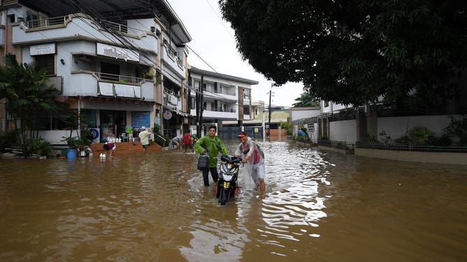 Residents push their motorcycle through a flooded street following heavy rains brought about by Tropical Storm Yagi at a village in Cainta town, Rizal province, East of Manila on September 3, 2024. Floods and landslides killed 11 people after a fierce tropical storm dumped heavy rain on the Philippines for a second day, officials said September 2. (Photo by Ted ALJIBE / AFP) (Photo by TED ALJIBE/AFP via Getty Images)