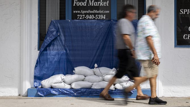 People walk past a restaurant with sandbags blocking the main entrance to prevent flood waters from getting into the building ahead of the arrival of Hurricane Helene in Tarpon Springs, Florida, on September 25, 2024. Thousands of residents on September 25 began evacuating parts of coastal Florida as the US state braces for Hurricane Helene, forecast to barrel ashore as a powerful, potentially deadly storm. Helene strengthened into a hurricane mid-morning in the Gulf of Mexico and is "expected to bring life-threatening storm surge, damaging winds, and flooding rains to a large portion of Florida and the Southeastern United States," the National Hurricane Center in Miami said in its latest bulletin. (Photo by Ricardo ARDUENGO / AFP) (Photo by RICARDO ARDUENGO/AFP via Getty Images)