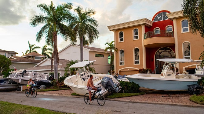 Cyclists pass a home on Friday, September 27, 2024, on Treasure Island, Florida, where several boats washed up in the front yard during Hurricane Helene.