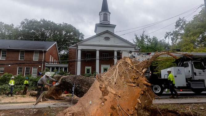 A crew works to use a chainsaw to remove a large tree that fell on McClendon Avenue NE across from the Neighborhood Church in the Candler Park neighborhood of Atlanta, Georgia, on Friday, September 27, 2024.