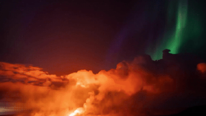 This image shows the Northern Lights shining bright as lava from a volcanic eruption in Iceland shoots high into the air.