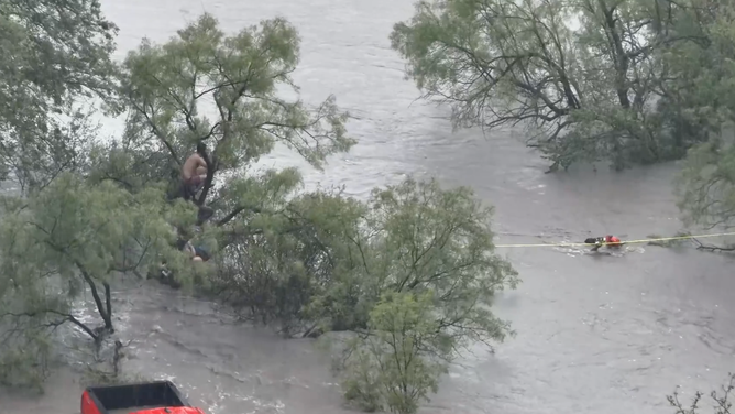 Rescuing deputies move across the flood current to reach the individuals.