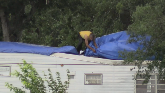 Man places tarp on mobile home.