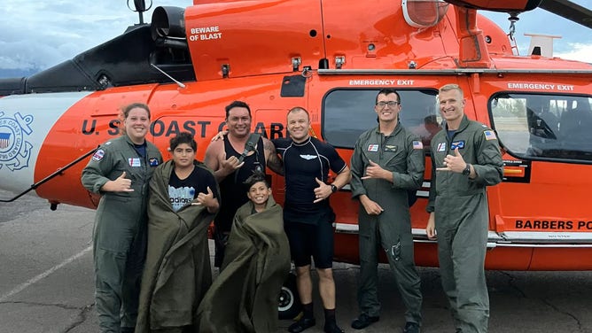 A man and his two sons smile at the camera along with the helicopter crew and rescue swimmer who saved them from their capsized boat.