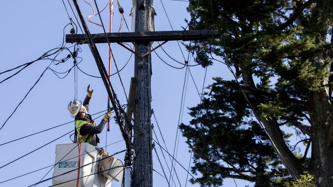 FILE: PG&E employee works to deactivate power lines in order to repair others knocked down by a trees due to high winds in Oakland, Calif.