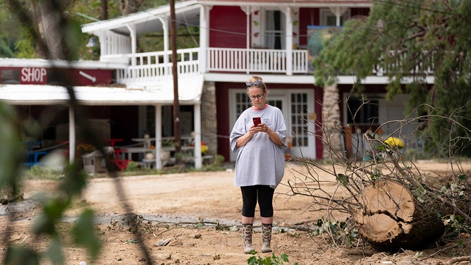 Marie O'Neal looks at her smartphone in the aftermath of Hurricane Helen at the Batcave in North Carolina on October 1, 2024.