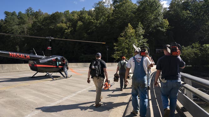 BAT CAVE, NORTH CAROLINA - OCTOBER 2: Men with chainsaws walk paste a helicopter on a bridge in the aftermath of Hurricane Helene on October 1, 2024 near Bat Cave, North Carolina. The death toll has topped 180 people across the southeastern U.S. due to the storm, according to published reports, which made landfall as a category 4 storm on Thursday. Millions are without power and the federal government has declared major disasters in areas of North Carolina, Florida, South Carolina, Tennessee, Georgia, Virginia and Alabama, freeing up federal emergency management money and resources for those states, according to the reports. (Photo by Sean Rayford/Getty Images)