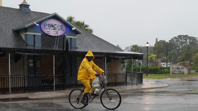 A man in rain gear rides a bike through Dunedin ahead of Hurricane Milton's expected landfall tonight on October 9, 2024 in Florida. Milton regained power on October 8 to become a Category 5 storm with maximum sustained winds of 165 mph (270 kph) as it barrels towards the west-central coast of Florida and is forecast to make landfall late October 9, according to the National Hurricane Center. (Photo by Bryan R. SMITH / AFP) (Photo by BRYAN R. SMITH/AFP via Getty Images)