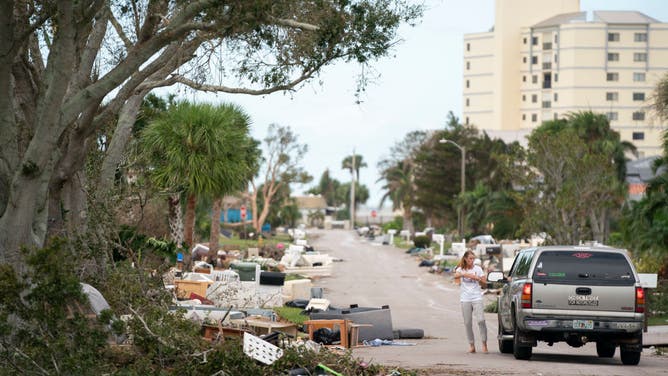 A woman talks to a motorist on a street littered with storm debris from Hurricane Helene and Hurricane Milton in the aftermath of Hurricane Milton on October 10, 2024 in Venice, Florida. Hurricane Milton made landfall as a Category 3 hurricane in the Siesta Key area.