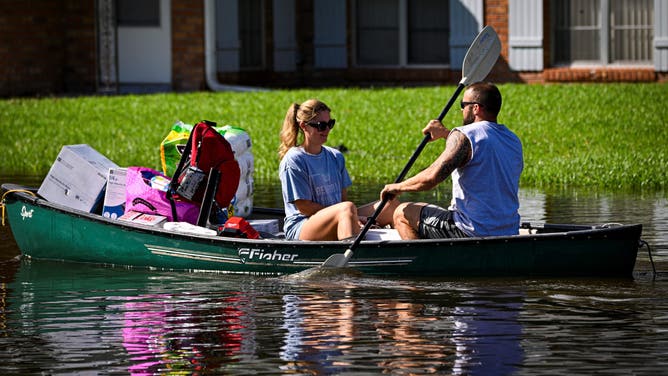 People paddle down a flooded street in South Daytona, Florida, following the passage of Hurricane Milton on October 11, 2024. The death toll from Hurricane Milton rose to at least 16 on Friday, officials in Florida said, as residents began the painful process of piecing their lives and homes back together. Nearly 2.5 million households and businesses were still without power, and some areas in the path cut through the Sunshine State by the monster storm from the Gulf of Mexico to the Atlantic Ocean remained flooded. (Photo by Miguel J. Rodriguez Carrillo / AFP) (Photo by MIGUEL J. RODRIGUEZ CARRILLO/AFP via Getty Images)