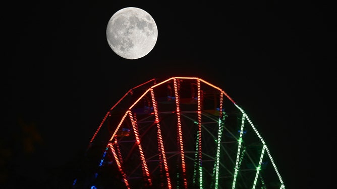 The full Hunter's Moon rises in the night sky over a Ferris wheel in Weihai, China's Shandong Province, on October 16, 2024.