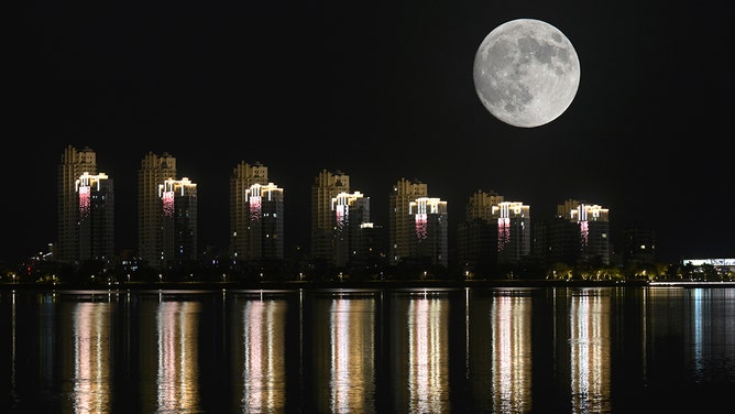 The full hunter's moon rises in the night sky over buildings on October 16, 2024 in Weihai, Shandong Province of China.