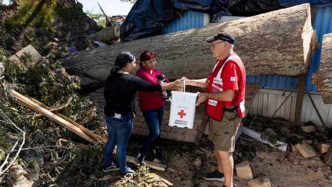 Hermila Contreras Ortiz and her daughter, Yajahira Guadalupe Gonzales Contreras receive a clean-up kit from Red Cross volunteer Richard Kimball in Swannanoa, North Carolina, after Hurricane Helene.