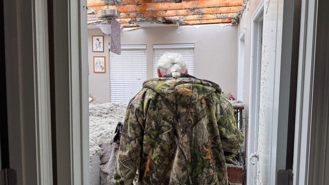 A man walks through his home in Prairie Grove, Ark., after storms ripped the roof off of the house.