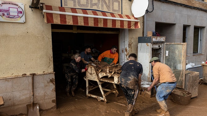 2024年10月31日、スペインのバレンシア州ウティエルで、大雨と洪水に続く最近の鉄砲水が国の大部分に影響を及ぼした後、パン屋のテーブルを捨てる人々。