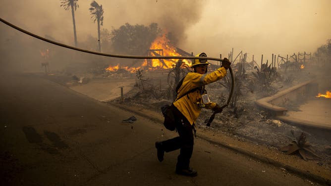 A firefighter pulls a hose in front of a burnt house as the Mountain Fire scorches acres in Camarillo Heights, Camarillo, California, on November 6, 2024.
