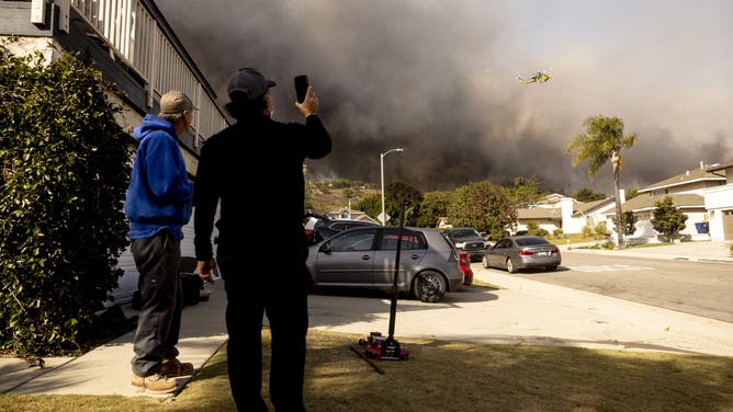 Residents watch a firefighting helicopter flying over the burning hills as the Santa Ana wind-fed Mountain fire scorches acres, in Camarillo, California, on November 6, 2024.