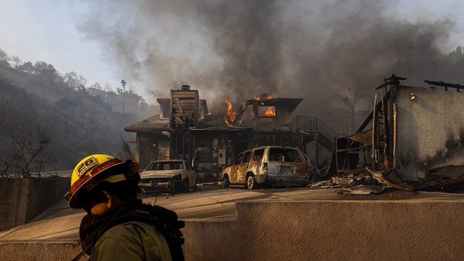 A firefighter walks past a house burning from the Mountain Fire on November 6, 2024 in Camarillo, California.