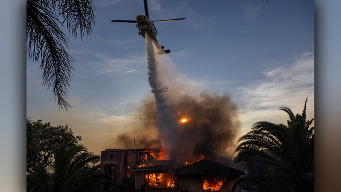 A helicopter drops fire retardant as a house burns in the Mountain Fire on November 6, 2024 in Camarillo, California.