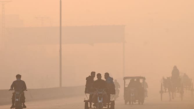 Commuters ride along a street engulfed in smog in Lahore on November 18, 2024.