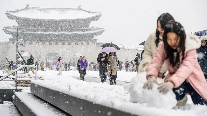 Pedestrians walk in front of the Gyeongbokgung Palace amid heavy snowfall in central Seoul on November 27, 2024.