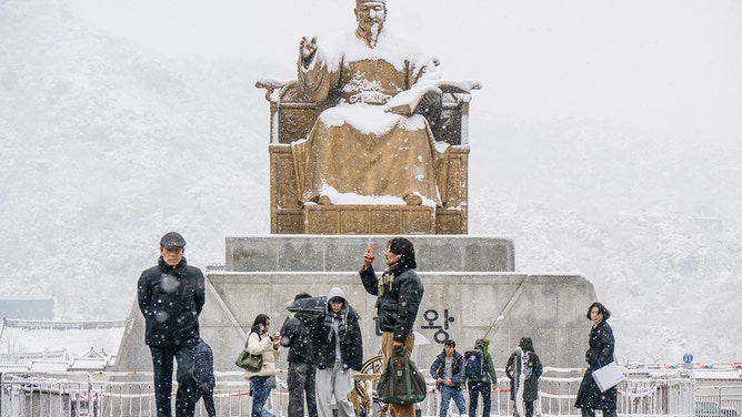 People walk in front of the Statue of King Sejong the Great, dedicated to the 15th Century Korean monarch, on Gwanghwamun Square amid heavy snowfall in central Seoul on November 27, 2024.