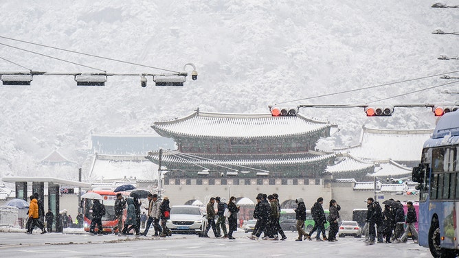 Pedestrians walk across a road in front of the Gyeongbokgung Palace amid heavy snowfall in central Seoul on November 27, 2024.