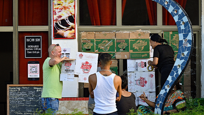 People protect the windows of a restaurant with cardboard ahead of Tropical Storm Rafael's arrival in Havana on November 5, 2024. Cuba was preparing for Tropical Storm Rafael, which is expected to make landfall on the island as a hurricane on November 6, intensifying the misery caused by a massive blackout and Hurricane Oscar. (Photo by ADALBERTO ROQUE/AFP) (Photo by ADALBERTO ROQUE/AFP via Getty Images)