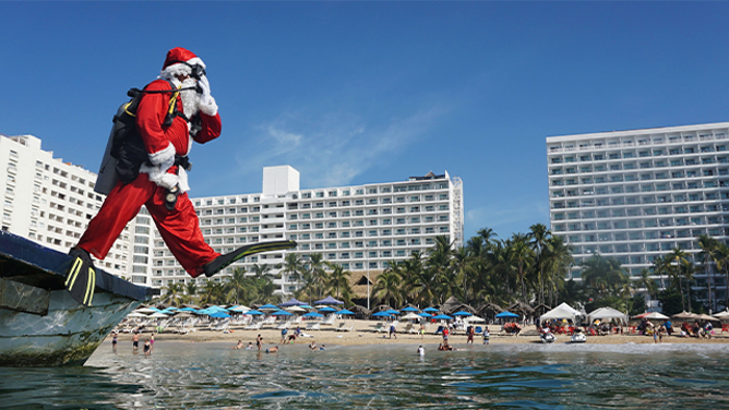 FILE - A man disguised as Santa Claus jumps into the water in the beach of Acapulco, state of Guerrero, Mexico, on December 21, 2021. (Photo by FRANCISCO ROBLES / AFP) (Photo by FRANCISCO ROBLES/AFP via Getty Images)