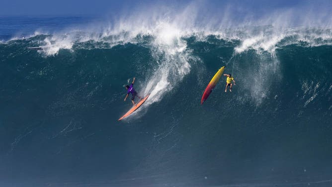 FILE – U.S. surfer Eli Olsen rides a wave as Hawaiian surfer Jake Maki gets wiped out during The Eddie Aikau Big Wave Invitational surfing contest on Jan. 22, 2023, at Waimea Bay on the North Shore of Oahu in Hawaii.