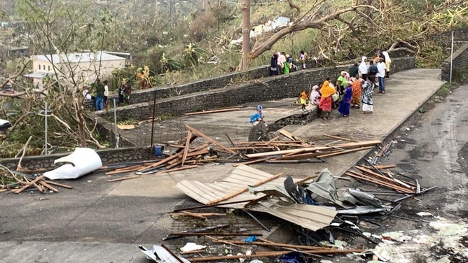 A photo taken on December 15, 2024 shows residents sitting by a road among piles of debris of metal sheets and wood after the cyclone Chido hit France's Indian Ocean territory of Mayotte.