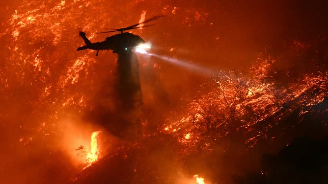 A fire fighting helicopter drops water as the Palisades fire grows near the Mandeville Canyon neighborhood and Encino, California, on January 11, 2025.