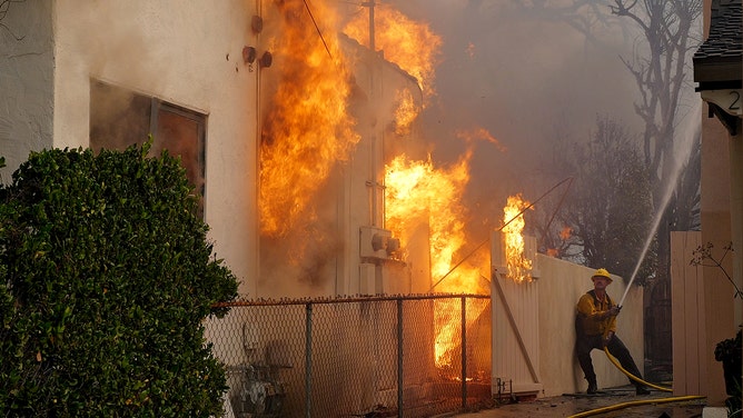 A firefighter sprays water on a house to protect it from the Eaton Fire in the Altadena neighborhood on January 08, 2025 in Pasadena, California.