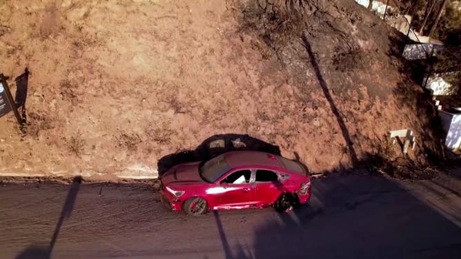 A red car sits parked on a street in Malibu after the Palisades Fire.