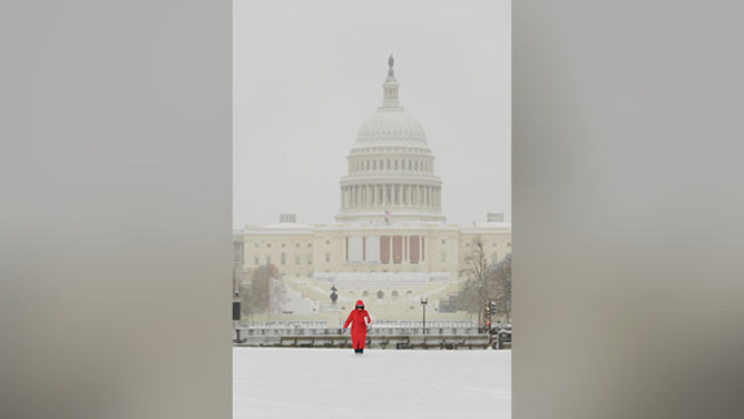 この写真は、2025年1月16日月曜日、冬の嵐の中、連邦議会議事堂を背景に雪の中を歩く人物を示しています。