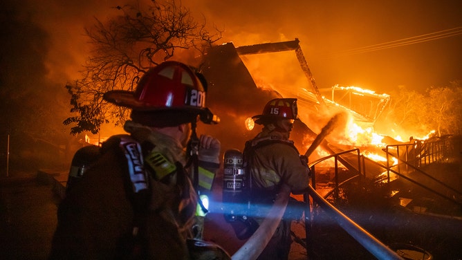 2025年1月8日、カリフォルニア州ロサンゼルスのパシフィック・パリセーズ地区で、大嵐の中、パリセーズ劇場を焼き尽くしたパリセーズ火災の炎と戦う消防士たち。