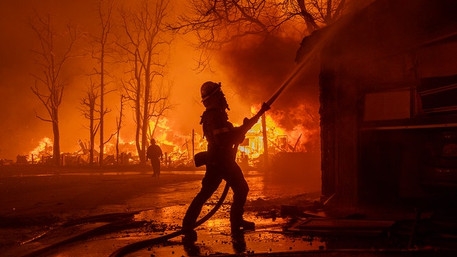 2025年1月7日、カリフォルニア州パサデナで複数の家が燃え、強風の中イートン火災と戦う消防士ら。