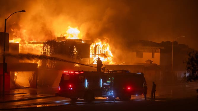 カリフォルニア州ロサンゼルス – 1月8日: 2025年1月8日、カリフォルニア州ロサンゼルスで、強力なハリケーンの最中にパシフィック・コースト・ハイウェイ沿いの家々を焼くパリセーズ火災と戦う消防士ら。南カリフォルニアのサンタアナの強風と乾燥した状況の中、急速に進行する山火事が2,900エーカー以上に広がり、沿岸地域の住宅を脅かしている。